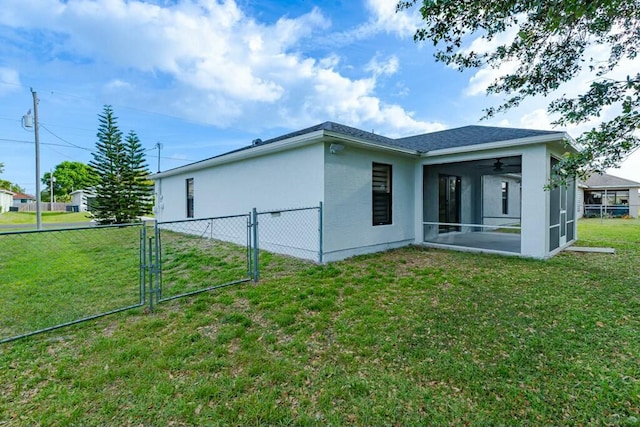 rear view of house featuring fence, a sunroom, a lawn, a gate, and stucco siding