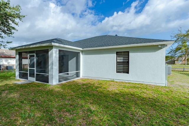 back of house with stucco siding, a shingled roof, a lawn, a sunroom, and fence