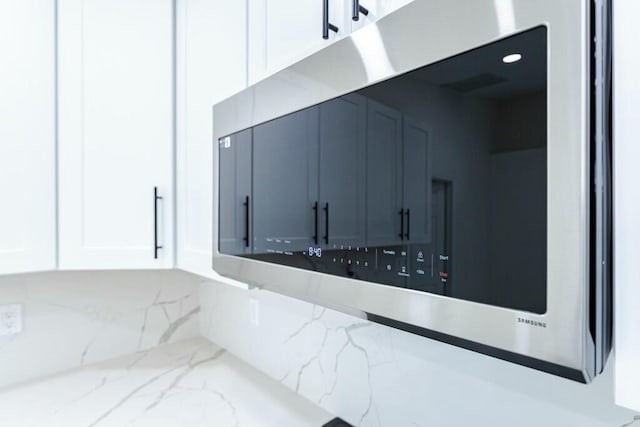 interior details with light stone counters, stainless steel microwave, recessed lighting, and white cabinets