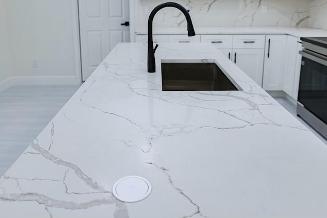 details featuring white cabinets, light stone counters, stove, wood finished floors, and a sink