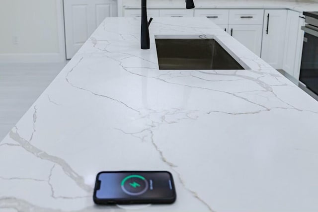 interior details with light stone countertops, stove, white cabinets, a sink, and wood finished floors