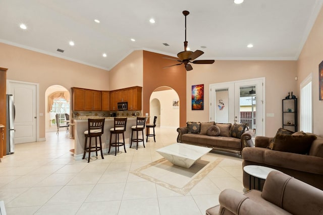 living room with light tile patterned floors, arched walkways, crown molding, high vaulted ceiling, and ceiling fan