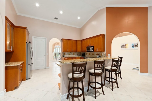 kitchen featuring arched walkways, appliances with stainless steel finishes, light stone counters, and a peninsula