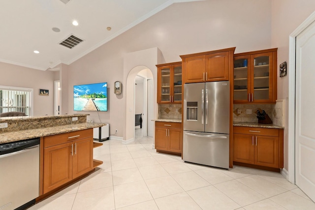 kitchen with backsplash, visible vents, arched walkways, brown cabinetry, and appliances with stainless steel finishes
