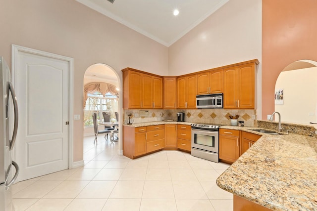 kitchen with stainless steel appliances, a towering ceiling, arched walkways, and a sink