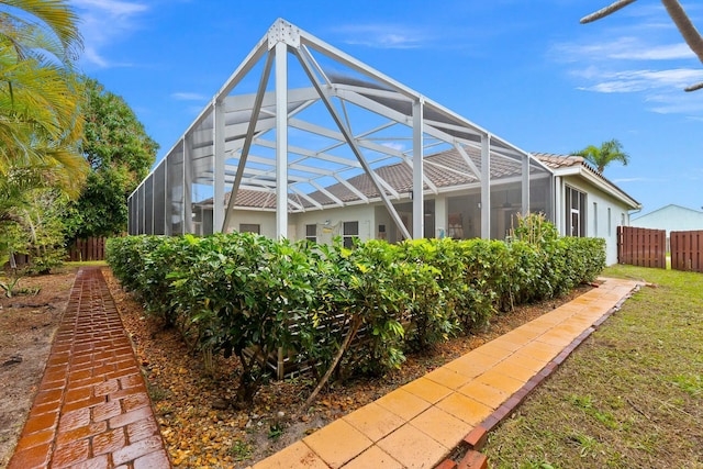 rear view of house with stucco siding, fence, a tiled roof, and glass enclosure