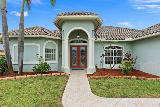 doorway to property featuring stucco siding, a yard, a tiled roof, and french doors
