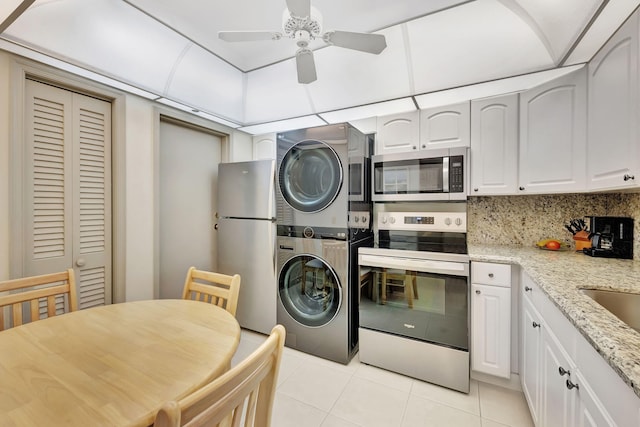 kitchen with light stone counters, light tile patterned flooring, stainless steel appliances, white cabinets, and stacked washing maching and dryer