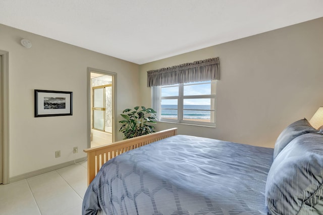 bedroom with a water view, ensuite bath, light tile patterned flooring, and baseboards