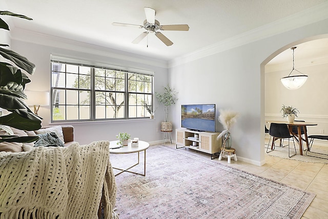 living area with arched walkways, crown molding, light tile patterned floors, ceiling fan, and baseboards