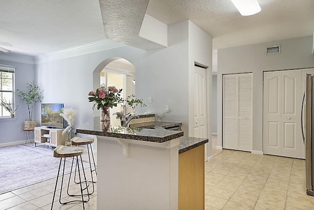 kitchen with light tile patterned floors, visible vents, dark countertops, a kitchen breakfast bar, and a textured ceiling