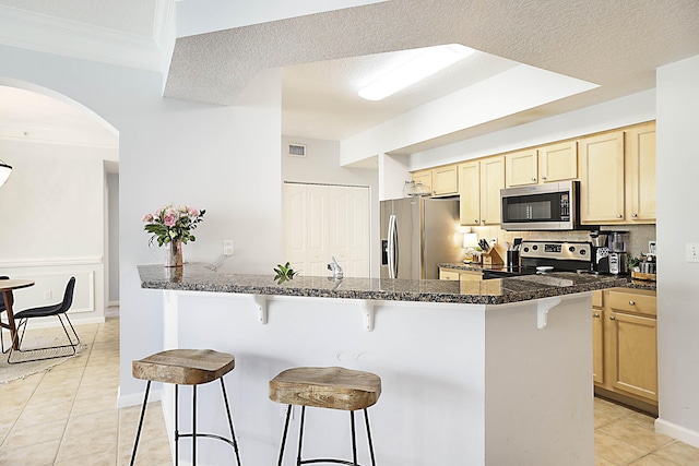 kitchen with appliances with stainless steel finishes, light brown cabinets, dark stone countertops, and a kitchen breakfast bar