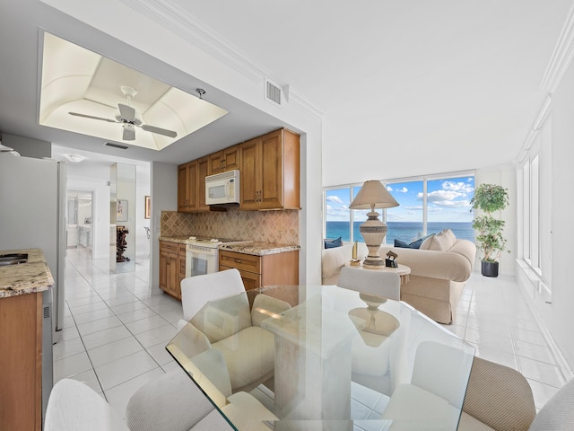 dining room with light tile patterned floors, a tray ceiling, a water view, and visible vents