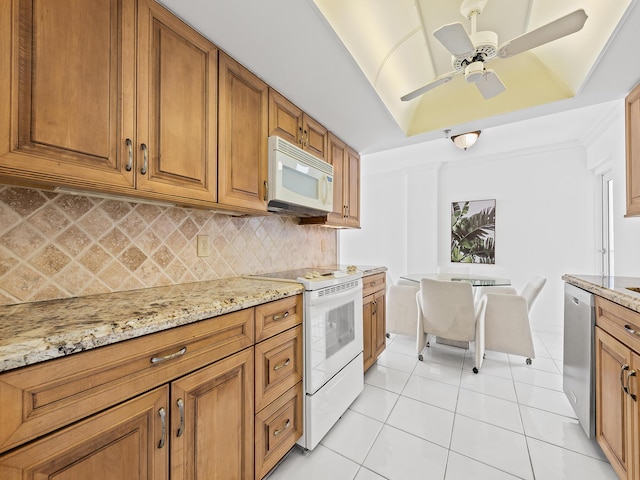 kitchen with tasteful backsplash, a raised ceiling, brown cabinetry, light stone countertops, and white appliances