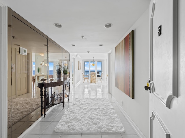 hallway featuring a notable chandelier, baseboards, and light tile patterned floors