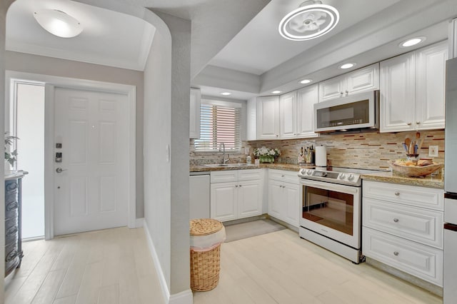 kitchen with arched walkways, a sink, white cabinetry, appliances with stainless steel finishes, and backsplash