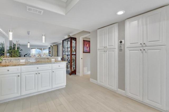 kitchen with light stone counters, visible vents, white cabinetry, light wood finished floors, and decorative light fixtures