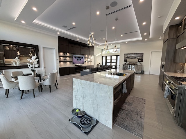 kitchen with high end stainless steel range, modern cabinets, a raised ceiling, and a large island with sink