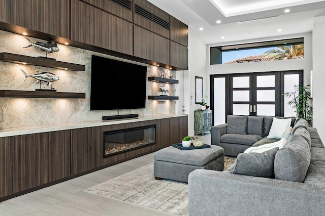 living room featuring french doors, light wood-type flooring, a glass covered fireplace, and recessed lighting