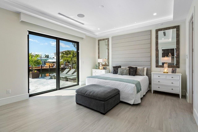 bedroom featuring access to exterior, baseboards, a raised ceiling, and wood finished floors