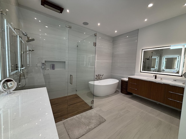 bathroom with tile walls, recessed lighting, a shower stall, vanity, and a freestanding tub