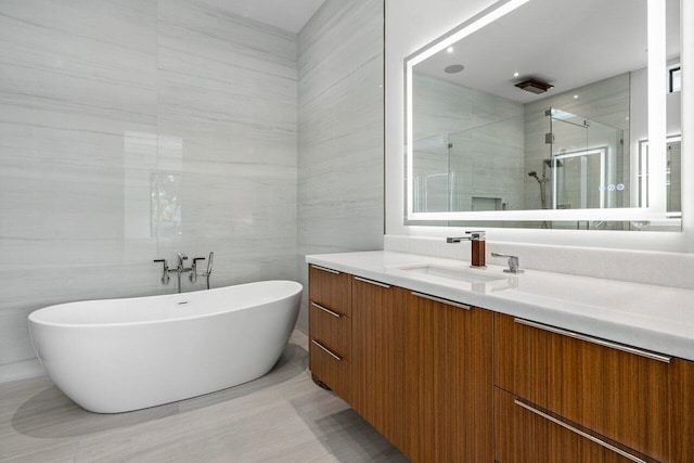 full bath with a stall shower, a freestanding bath, vanity, and tile walls