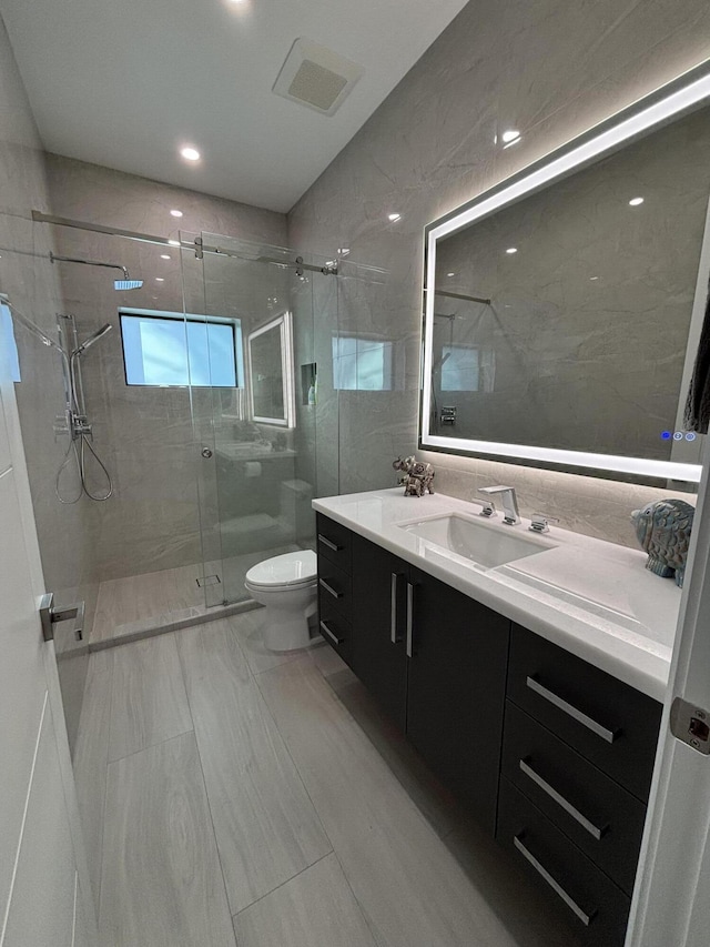 full bath with toilet, tile walls, vanity, visible vents, and a shower stall