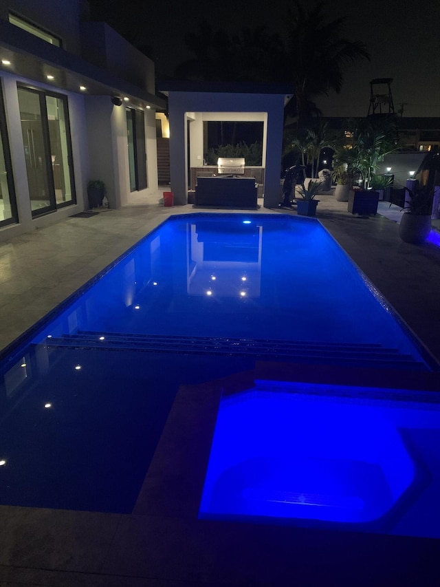 pool at night featuring exterior kitchen, a patio area, and an outdoor pool