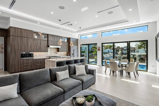 living room with light wood-style floors, recessed lighting, a raised ceiling, and a healthy amount of sunlight