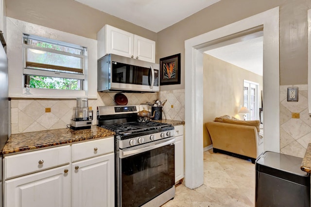 kitchen featuring appliances with stainless steel finishes, dark stone counters, white cabinetry, and backsplash