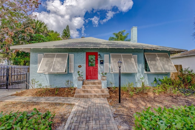 bungalow-style house with a chimney, fence, and stucco siding