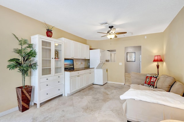 kitchen featuring stacked washer / drying machine, visible vents, glass insert cabinets, white cabinets, and ceiling fan