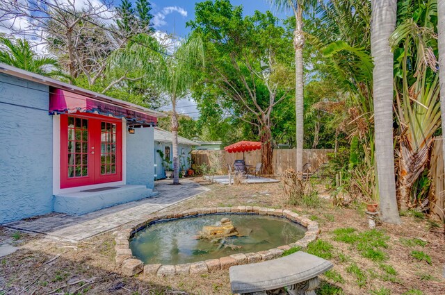 view of yard featuring a patio, french doors, a fenced backyard, and a garden pond