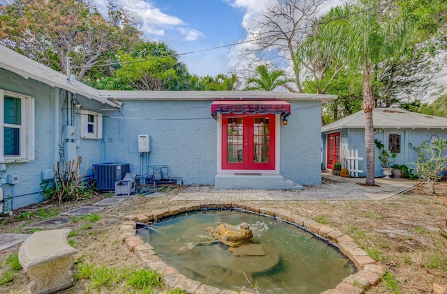 exterior space with central AC unit, french doors, a small pond, stucco siding, and a patio area