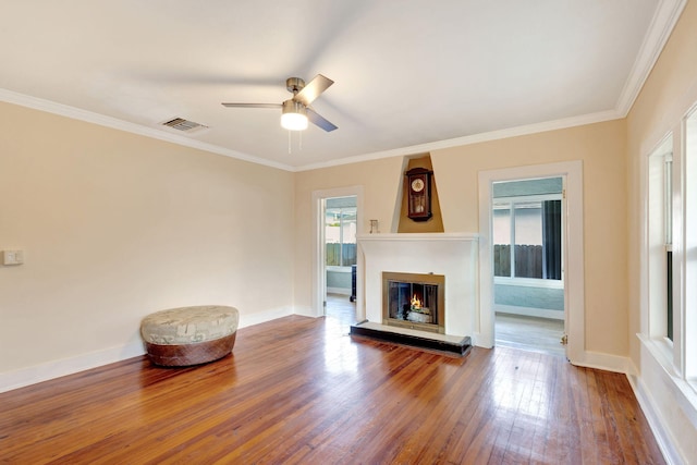 unfurnished living room with ornamental molding, plenty of natural light, a glass covered fireplace, and hardwood / wood-style flooring