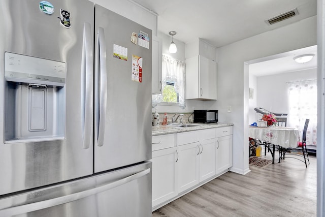 kitchen with black microwave, a sink, visible vents, light countertops, and stainless steel refrigerator with ice dispenser