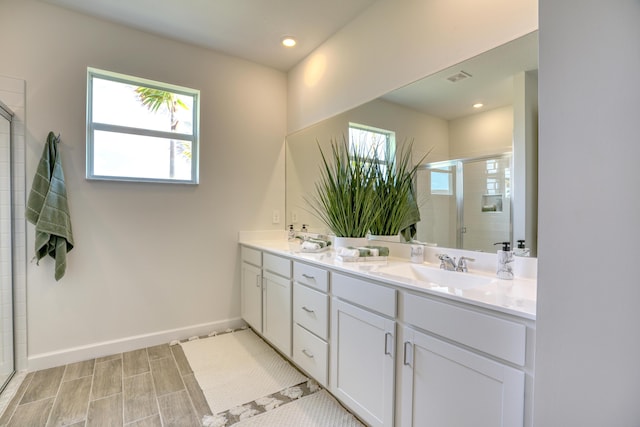 bathroom with double vanity, visible vents, a sink, a shower stall, and baseboards