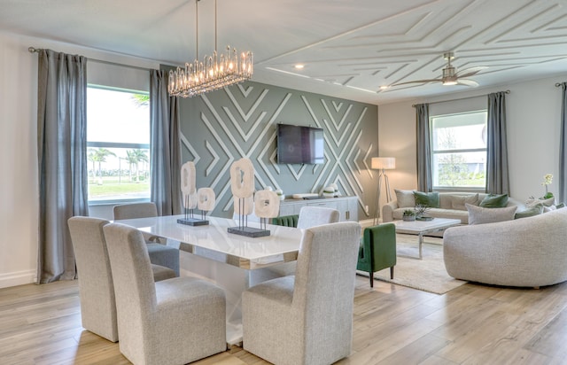 dining room featuring ceiling fan with notable chandelier, an accent wall, light wood finished floors, and baseboards