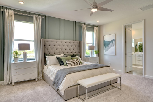 bedroom with light carpet, visible vents, baseboards, ensuite bath, and ceiling fan