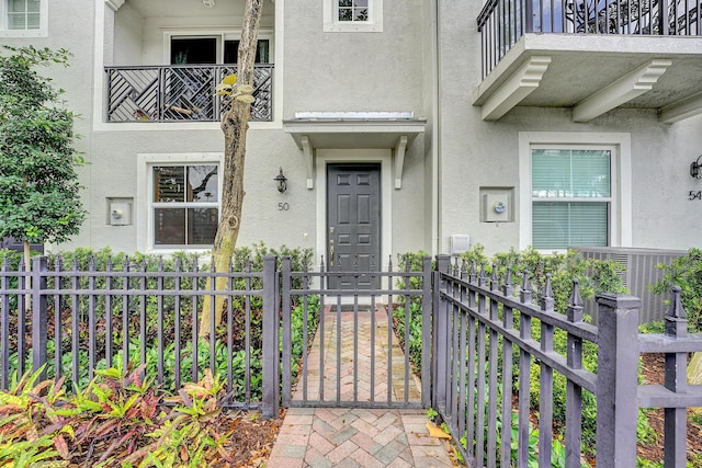 property entrance featuring fence, a balcony, and stucco siding