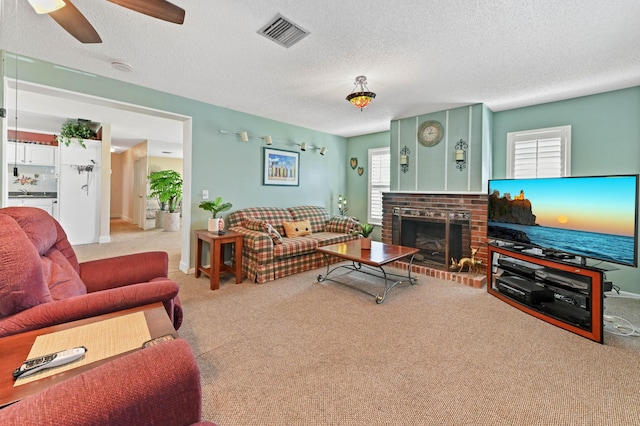 carpeted living room featuring a ceiling fan, visible vents, a fireplace, and a textured ceiling