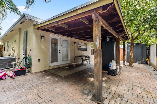 view of patio / terrace featuring a storage shed, an outbuilding, fence, french doors, and central AC