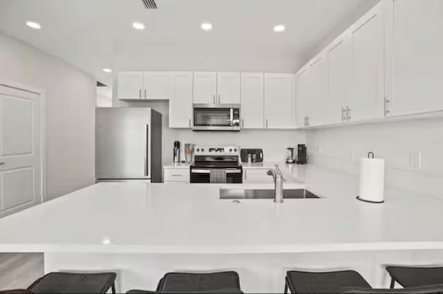 kitchen featuring stainless steel appliances, white cabinets, a sink, and a kitchen breakfast bar