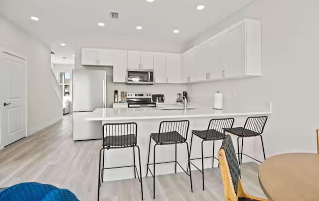 kitchen featuring appliances with stainless steel finishes, a peninsula, light countertops, white cabinetry, and a sink