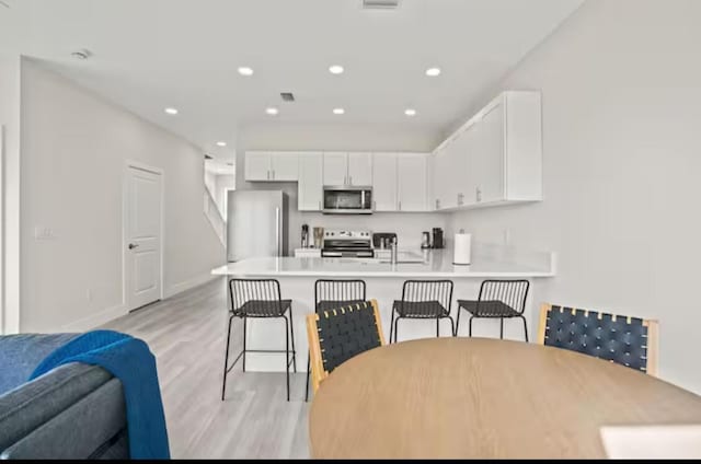 kitchen with appliances with stainless steel finishes, a peninsula, light countertops, a kitchen bar, and white cabinetry