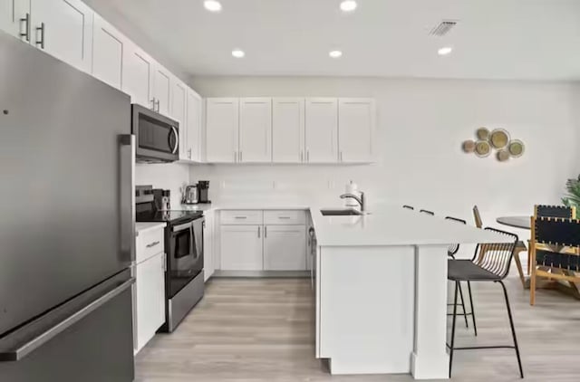 kitchen with appliances with stainless steel finishes, light countertops, white cabinetry, and a kitchen breakfast bar