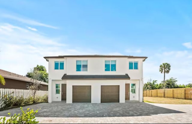 view of front facade featuring decorative driveway, fence, an attached garage, and stucco siding