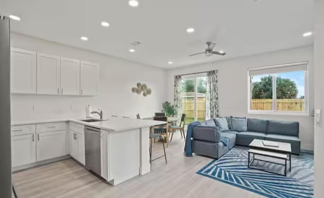 kitchen featuring stainless steel dishwasher, white cabinetry, open floor plan, and light countertops