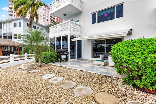 rear view of house featuring a patio area, fence, a balcony, and stucco siding