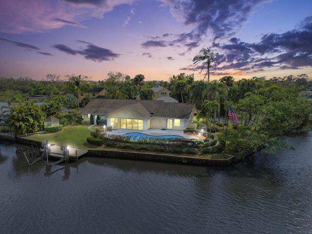 back of property at dusk featuring a water view, an outdoor pool, and a patio